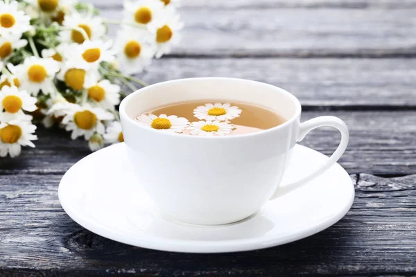 灰色の木製テーブルにカモミールの花とお茶のカップ — ストック写真