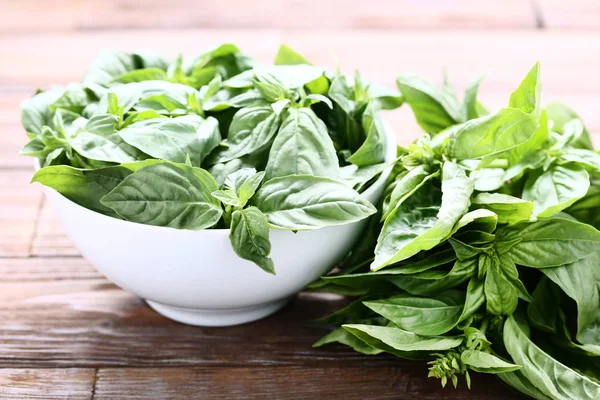 Green basil leafs in bowl on brown wooden table — Stock Photo, Image