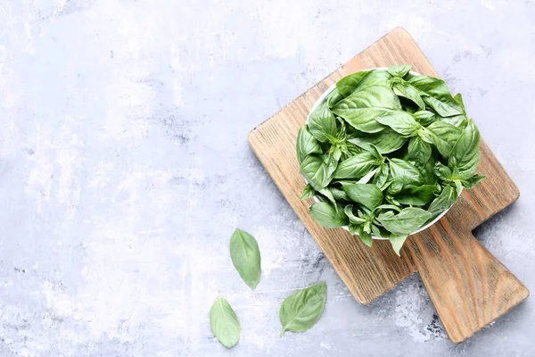 Green basil leafs in bowl with cutting board on grey wooden tabl — Stock Photo, Image