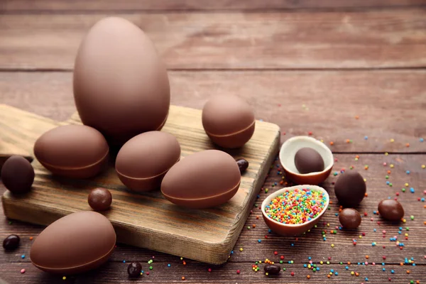 Uova di Pasqua al cioccolato con caramelle colorate su tavola di legno marrone — Foto Stock