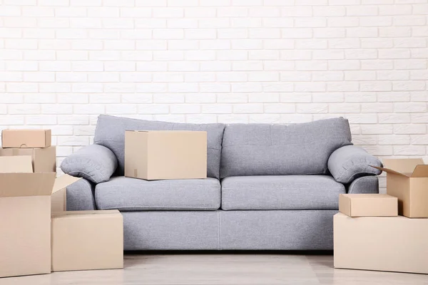 Kotak kardus dengan sofa abu-abu dengan latar belakang dinding bata — Stok Foto
