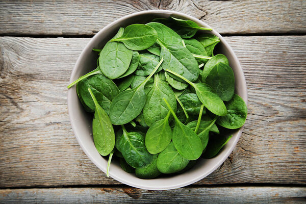 Spinach leafs in bowl on grey wooden table