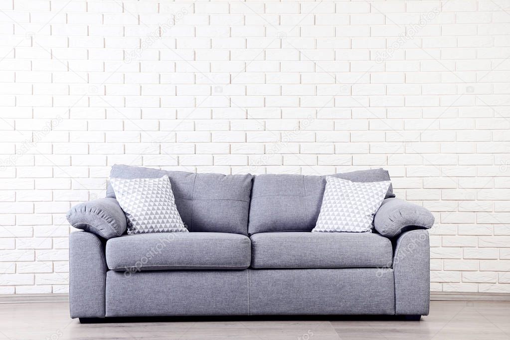Modern grey sofa with pillows on brick wall background