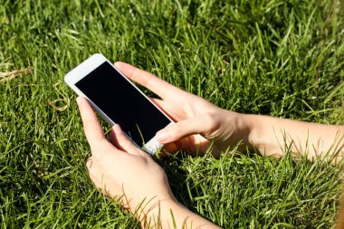 Holding ve yeşil çimenlerin üzerinde smartphone kullanarak kadın