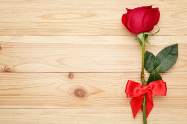 Kahverengi ahşap masa üzerinde şerit yay ile kırmızı gül