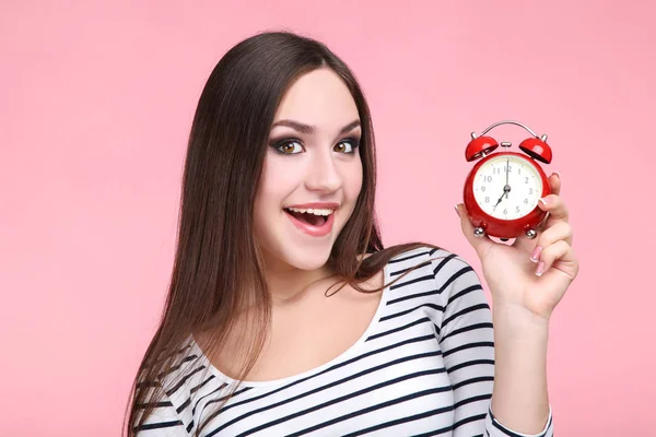 Bella giovane donna con sveglia rossa su sfondo rosa — Foto Stock