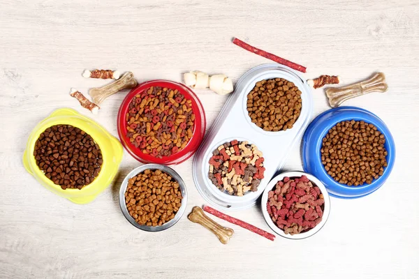 Сухой корм для домашних животных в мисках с костями на полу — стоковое фото