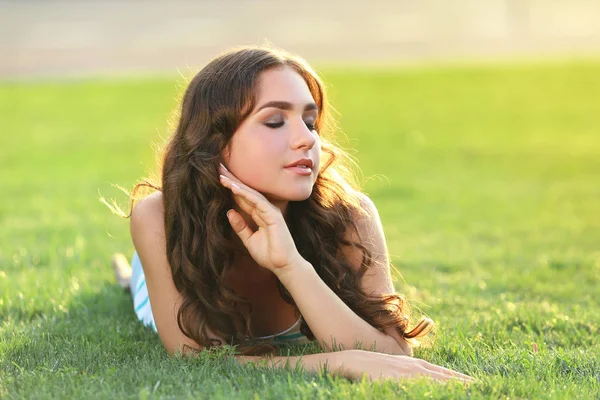Ung kvinna liggande på grönt gräs i parken — Stockfoto