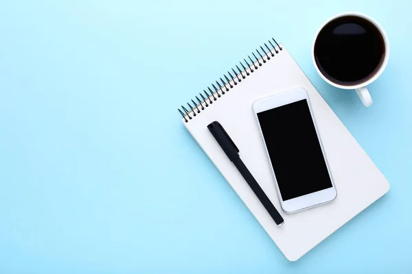 Smartphone med kopp kaffe och anteckningsbok på blå bakgrund — Stockfoto