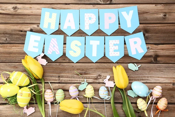 Tulipanes amarillos con huevos, conejos pequeños y texto Feliz Pascua en — Foto de Stock