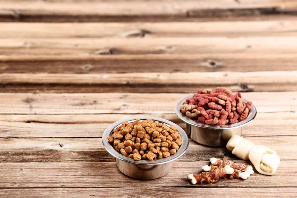 Сухой корм для домашних животных в мисках с костями на коричневом деревянном столе — стоковое фото