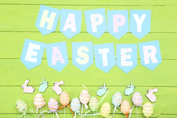 Pequeños conejos con huevos y texto Feliz Pascua en madera verde ta — Foto de Stock