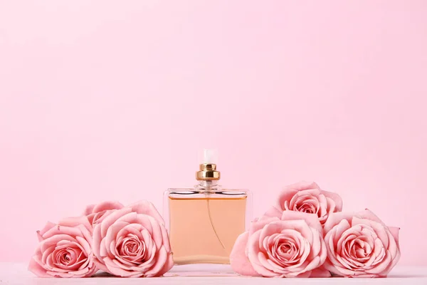 Бутылка духов с розами на розовом фоне — стоковое фото
