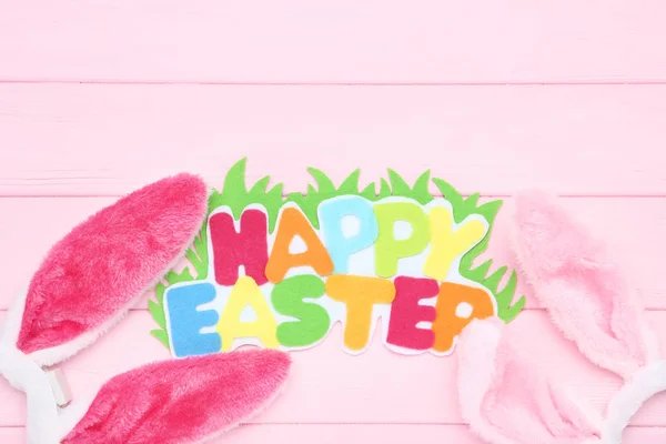 Orejas de conejo con texto Feliz Pascua en mesa de madera rosa — Foto de Stock