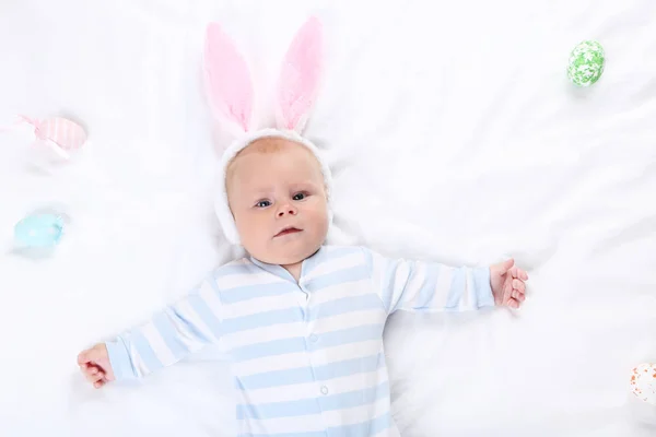 Chlapeček v králičí uši leží na bílé posteli — Stock fotografie