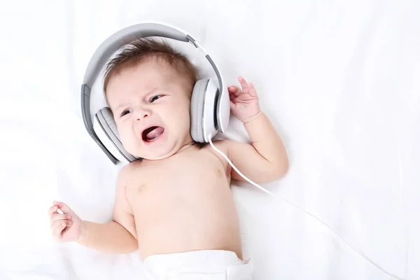 Cute baby ze słuchawkami, leżąc na łóżku biały — Zdjęcie stockowe