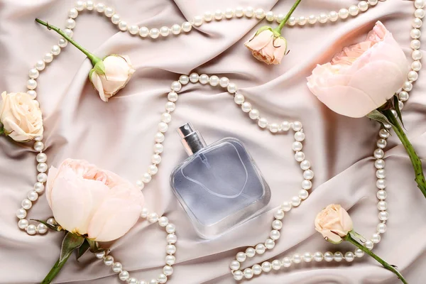 Parfümös üveg virágok és gyöngyök szatén háttér — Stock Fotó