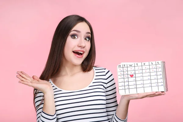 Bella giovane donna con calendario su sfondo rosa — Foto Stock