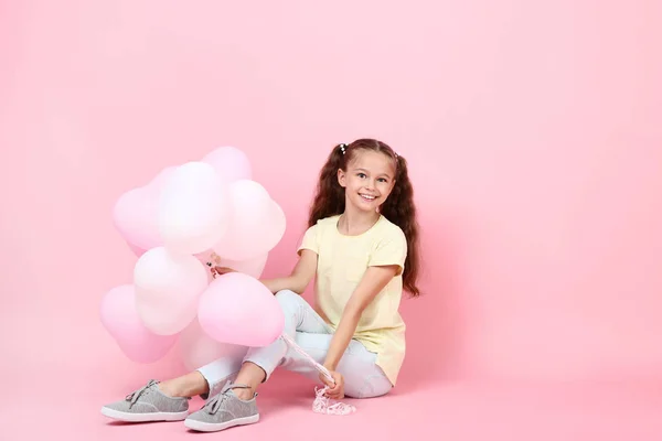 Cute young girl with balloons sitting on pink background — Stock Photo, Image
