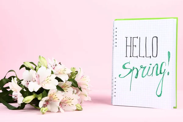 Alstroemeria flowers and notepad with text Hello Spring on pink