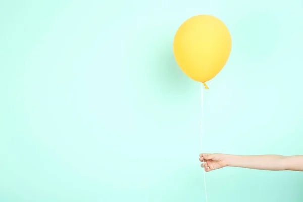 Kvinnliga handen håller gul ballong på mint bakgrund — Stockfoto