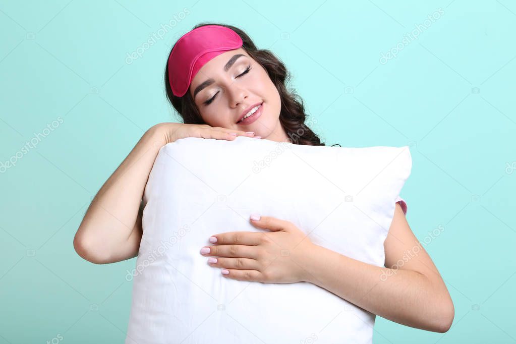 Beautiful girl with sleeping mask and white pillow on mint backg