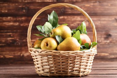 Kahverengi ahşap masada olgun armut ve yeşil yaprakların sepet