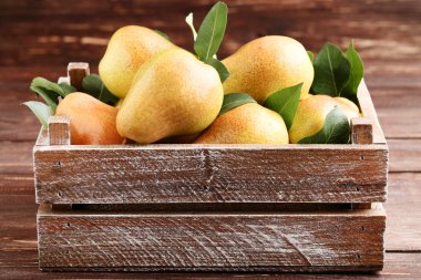 Kahverengi ahşap masa üzerinde sandıkta olgun armut ve yeşil yaprakların