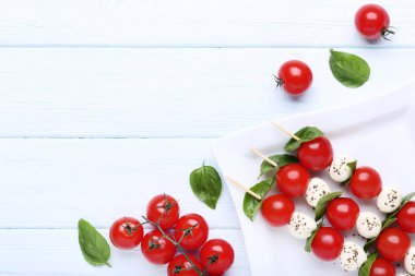 Mozzarella peyniri, domates ve fesleğen sopalarla yapraklar üzerinde ahşap masa