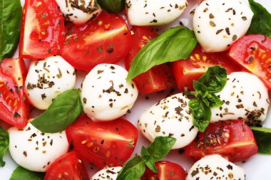 Mozzarella peyniri, domates ve fesleğen yaprakları beyaz plaka üzerinde