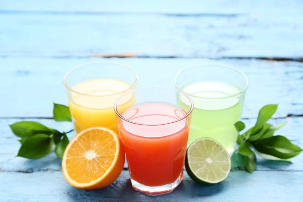 Citrus juice in glasses with fruits on blue wooden table — Stock Photo, Image