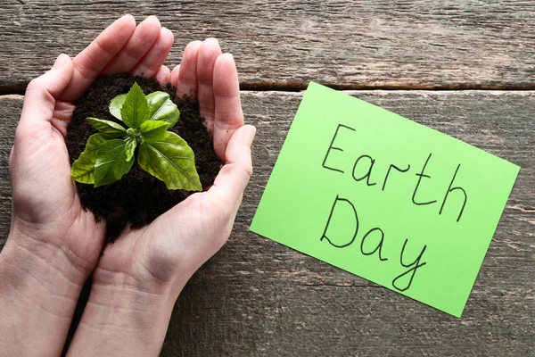 Female hands holding young plant with inscription Earth Day on p — Stock Photo, Image