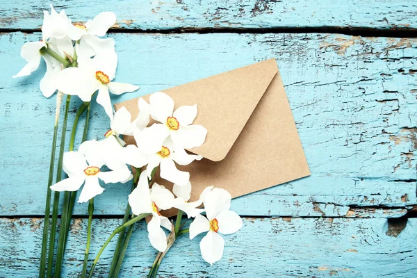 White narcissus flowers with envelope on blue wooden table — Stock Photo, Image