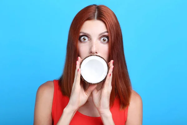 Hermosa mujer pelirroja con fruta de coco sobre fondo azul — Foto de Stock