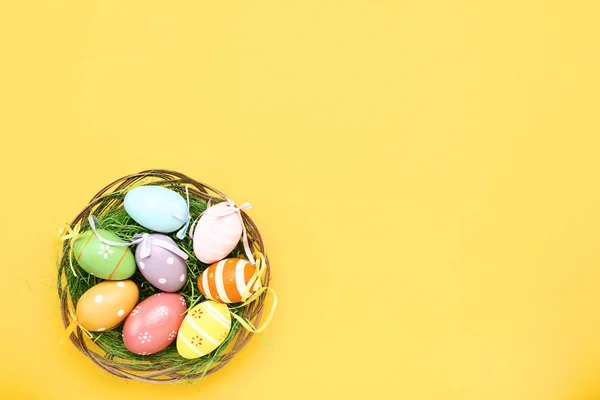 Ovos de páscoa coloridos na cesta no fundo amarelo — Fotografia de Stock
