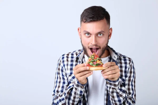 Ung man äta pizza på grå bakgrund — Stockfoto