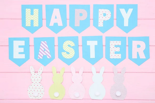 Conejos de papel con texto Feliz Pascua en mesa de madera rosa — Foto de Stock