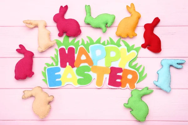 Conejos de tela con texto Feliz Pascua en mesa de madera rosa — Foto de Stock