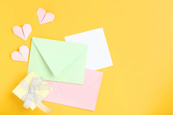 Sarı arka planda hediye kutusu ve Kağıt kalpleri olan zarflar — Stok fotoğraf