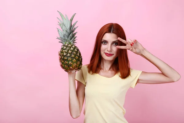 Jonge roodharige vrouw met ananas op roze achtergrond — Stockfoto