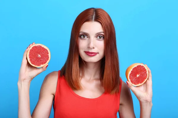 Mooie roodharige vrouw met grapefruit op blauwe achtergrond — Stockfoto