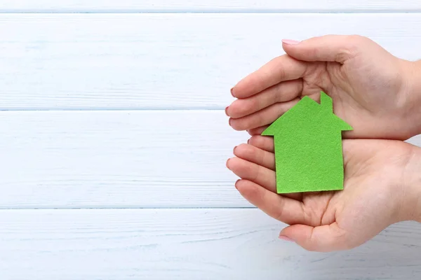 Руки женщины держат зеленый бумажный дом на деревянном фоне — стоковое фото