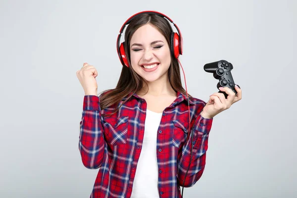 Bella ragazza con joystick e cuffie su sfondo grigio — Foto Stock