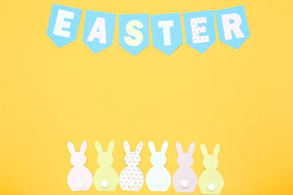 Conejos de papel con palabra Pascua sobre fondo amarillo — Foto de Stock