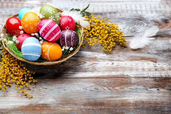 Ovos de páscoa coloridos na cesta com flores na mesa de madeira marrom — Fotografia de Stock