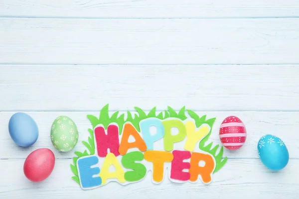 Huevos coloridos con texto Feliz Pascua en mesa de madera — Foto de Stock