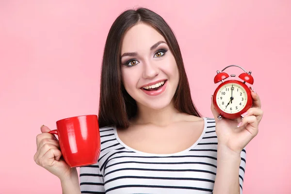 빨간색 알람 시계와 분홍색 배경에 컵 젊은 여자 — 스톡 사진