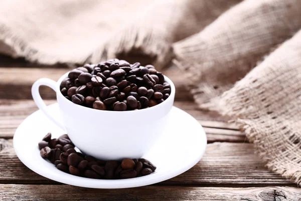 Granos de café en taza blanca sobre mesa de madera marrón — Foto de Stock