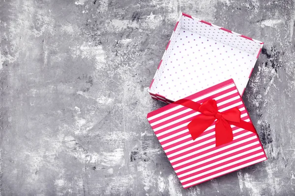 Open gift box with red bow on grey wooden table