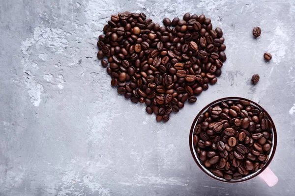Kahve çekirdekleri ile kupa gri ahşap masa üzerinde kalp şeklinde — Stok fotoğraf